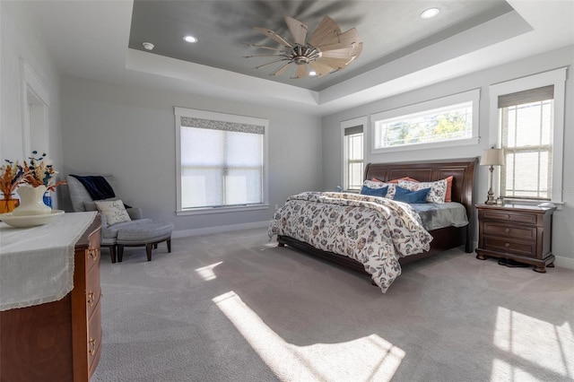 carpeted bedroom with ceiling fan and a tray ceiling