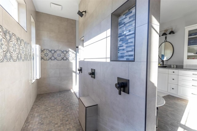 bathroom featuring tiled shower, vanity, and tile walls