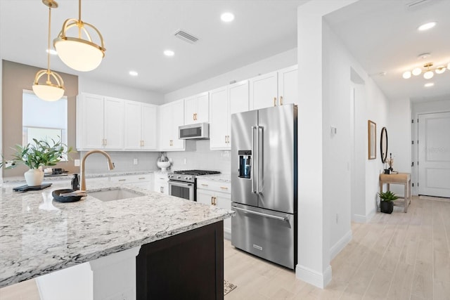 kitchen with sink, white cabinetry, decorative light fixtures, appliances with stainless steel finishes, and light stone countertops