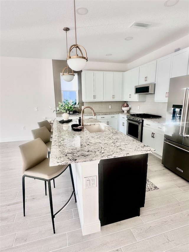 kitchen with sink, decorative light fixtures, an island with sink, stainless steel appliances, and white cabinets