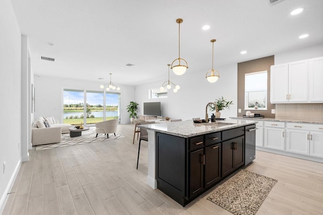 kitchen featuring white cabinetry, an island with sink, sink, hanging light fixtures, and light stone counters