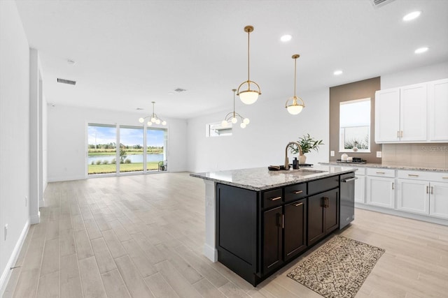 kitchen with sink, light stone counters, a center island with sink, pendant lighting, and white cabinets