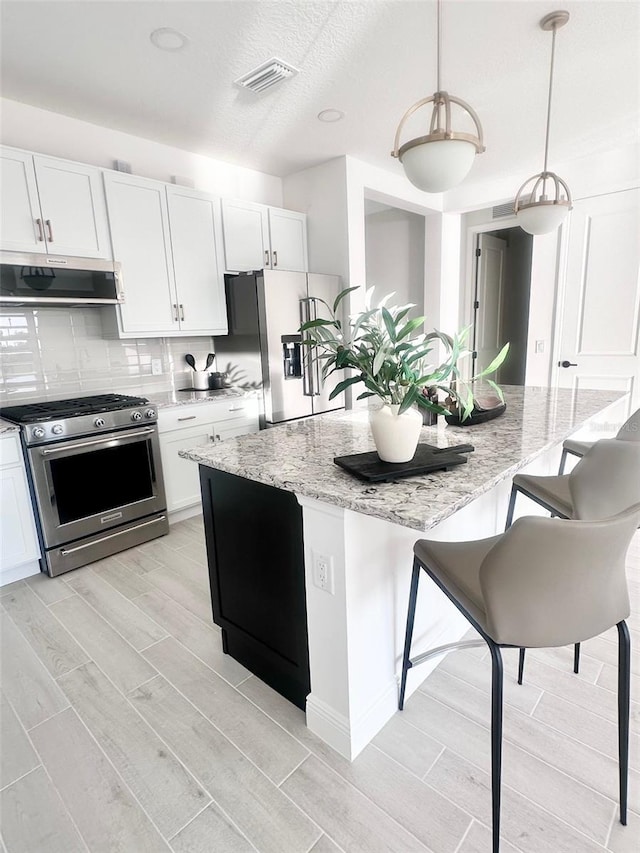 kitchen featuring white cabinetry, stainless steel appliances, ventilation hood, and hanging light fixtures