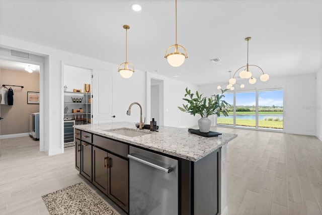 kitchen featuring sink, a water view, decorative light fixtures, light stone countertops, and a kitchen island with sink