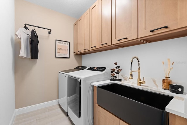 clothes washing area featuring sink, light wood-type flooring, cabinets, washer and clothes dryer, and a textured ceiling