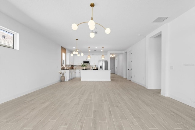 unfurnished living room featuring plenty of natural light, a chandelier, and light wood-type flooring