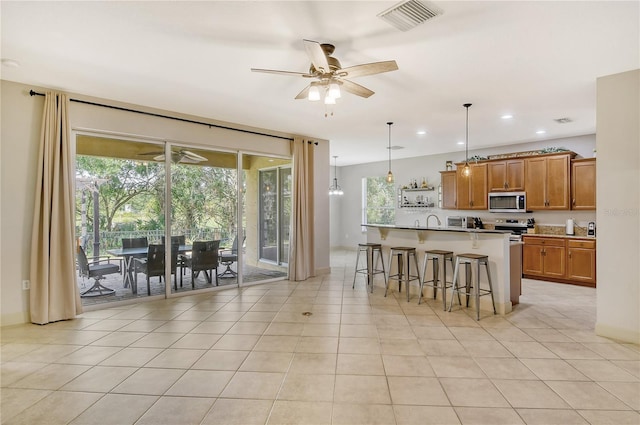 kitchen featuring appliances with stainless steel finishes, an island with sink, a kitchen breakfast bar, decorative light fixtures, and light tile patterned floors