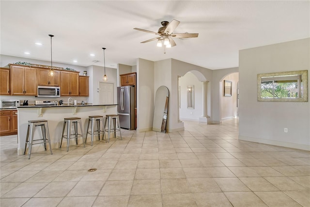 kitchen featuring hanging light fixtures, a center island with sink, ceiling fan, a breakfast bar, and stainless steel appliances