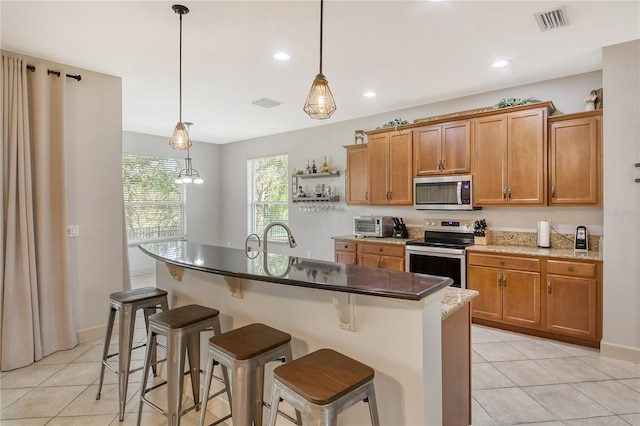 kitchen featuring a kitchen breakfast bar, an island with sink, stainless steel appliances, and pendant lighting