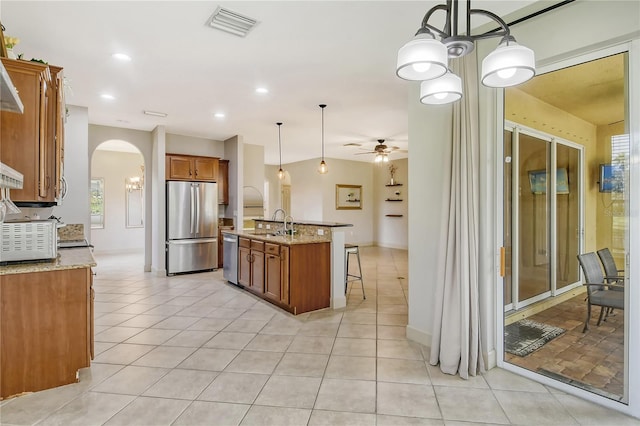 kitchen with a center island with sink, appliances with stainless steel finishes, light stone countertops, sink, and decorative light fixtures