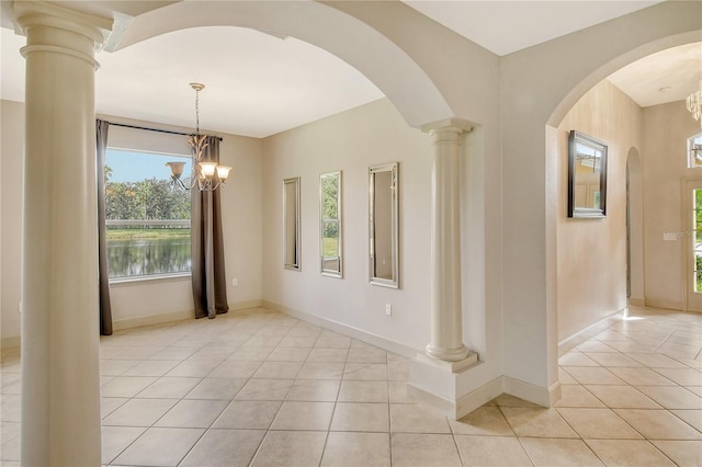 tiled empty room featuring a notable chandelier, a water view, and ornate columns