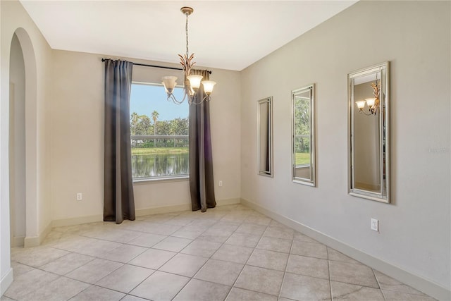 spare room featuring a wealth of natural light, a water view, an inviting chandelier, and light tile patterned floors