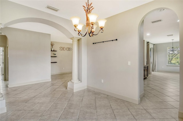 spare room featuring a chandelier, ornate columns, and light tile patterned floors