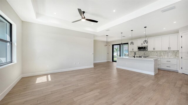 kitchen with a center island with sink, white cabinetry, hanging light fixtures, and light wood-type flooring