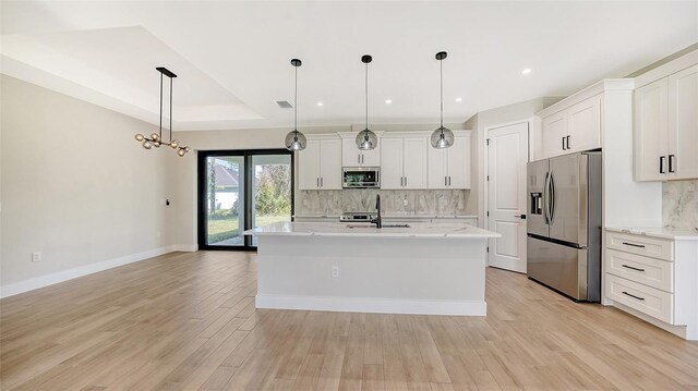 kitchen with appliances with stainless steel finishes, hanging light fixtures, light wood-type flooring, and an island with sink