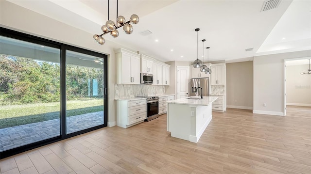 kitchen with light hardwood / wood-style flooring, an island with sink, stainless steel appliances, decorative light fixtures, and white cabinetry