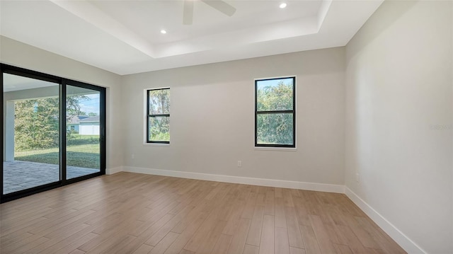 empty room featuring light hardwood / wood-style flooring, ceiling fan, and a raised ceiling