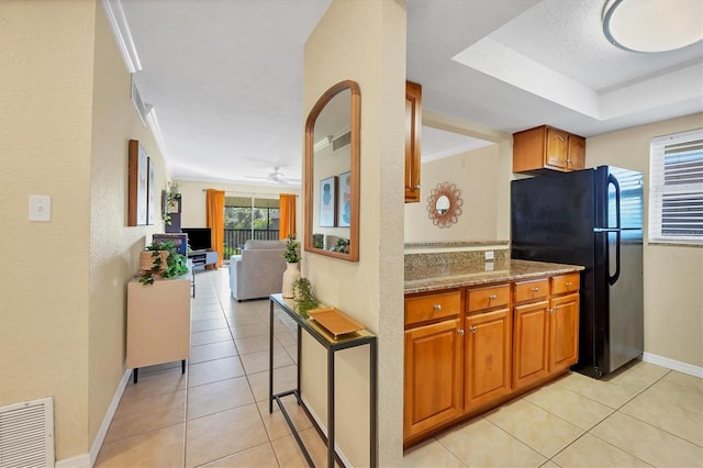 kitchen with light tile patterned floors, black fridge, ceiling fan, and light stone counters