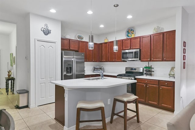 kitchen featuring pendant lighting, light tile patterned floors, a kitchen island with sink, appliances with stainless steel finishes, and a kitchen bar