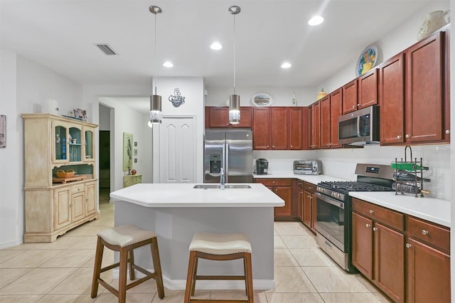 kitchen with a kitchen island with sink, stainless steel appliances, a breakfast bar, decorative light fixtures, and light tile patterned floors