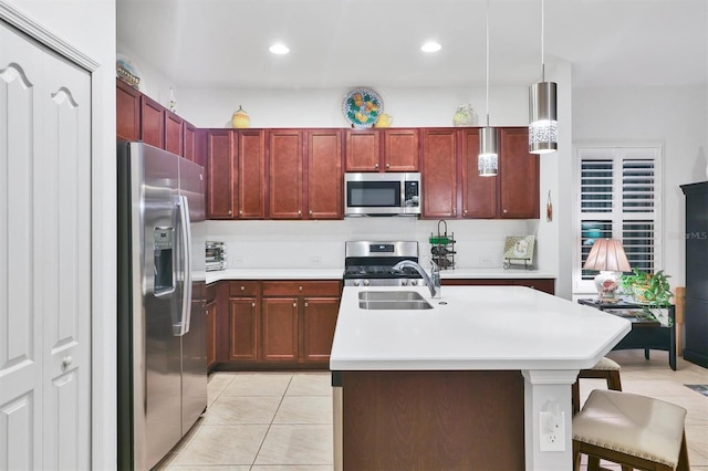 kitchen featuring sink, hanging light fixtures, appliances with stainless steel finishes, a kitchen bar, and a center island with sink