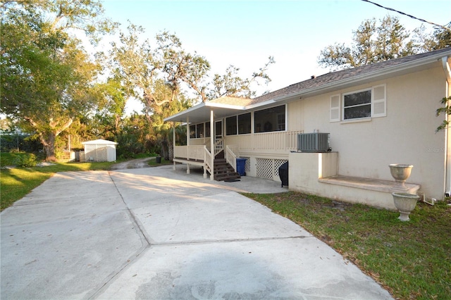 rear view of property with stucco siding, central air condition unit, concrete driveway, a sunroom, and an outdoor structure