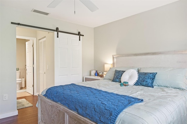 bedroom featuring ceiling fan, dark hardwood / wood-style floors, a barn door, connected bathroom, and a closet