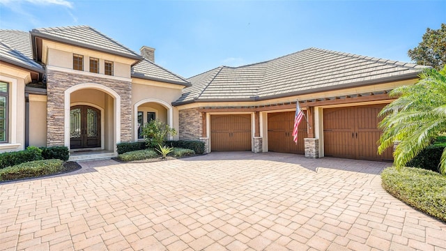 view of front of property with stucco siding, decorative driveway, stone siding, french doors, and an attached garage