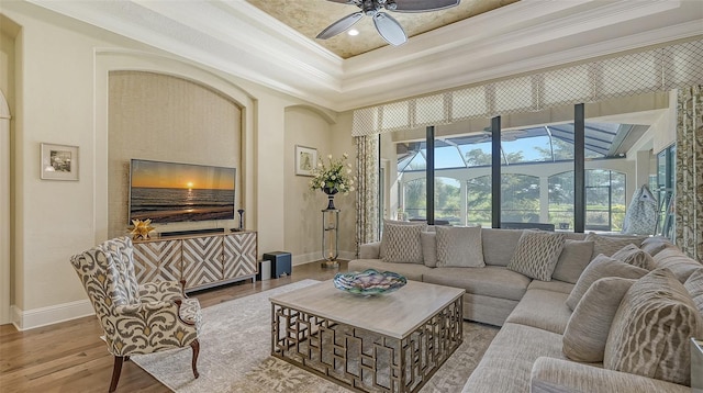 living room with a raised ceiling, crown molding, ceiling fan, and light wood-type flooring