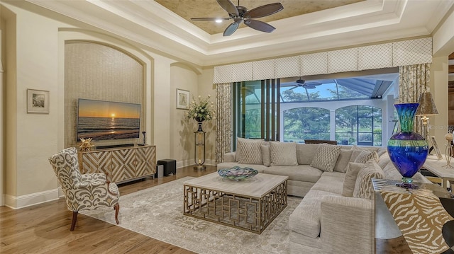 living room with wood-type flooring, a tray ceiling, and crown molding