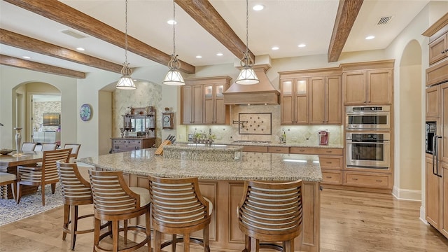 kitchen featuring decorative light fixtures, light hardwood / wood-style flooring, appliances with stainless steel finishes, beamed ceiling, and a large island