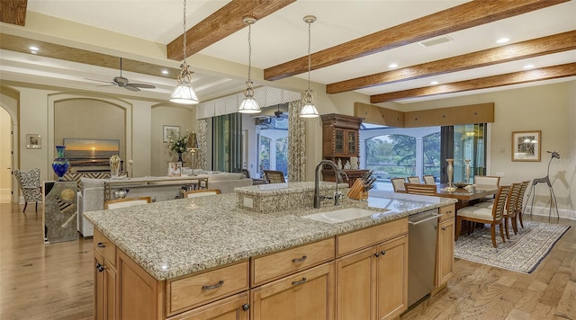 kitchen with beamed ceiling, light hardwood / wood-style flooring, sink, and an island with sink