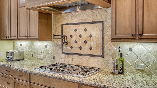 kitchen with tasteful backsplash, light stone counters, stainless steel gas stovetop, and custom exhaust hood