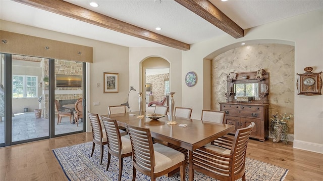 dining space with plenty of natural light, beamed ceiling, a textured ceiling, and light hardwood / wood-style flooring