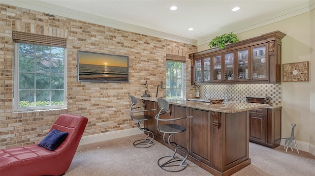 bar with a healthy amount of sunlight, light stone counters, dark brown cabinetry, and ornamental molding