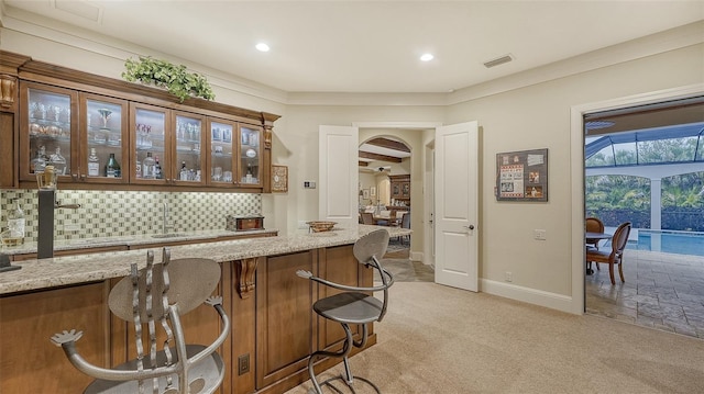 bar with decorative backsplash, light stone counters, and light colored carpet