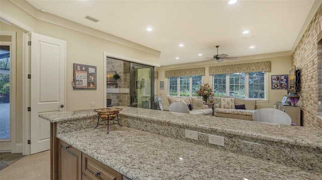 interior space with light carpet, light stone counters, brick wall, ceiling fan, and crown molding