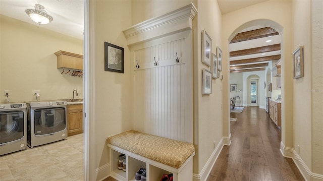 mudroom featuring beam ceiling, washing machine and clothes dryer, sink, and light hardwood / wood-style flooring