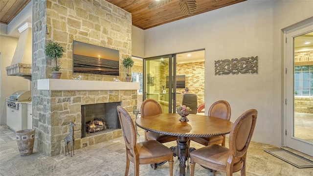 dining area with a stone fireplace and wood ceiling