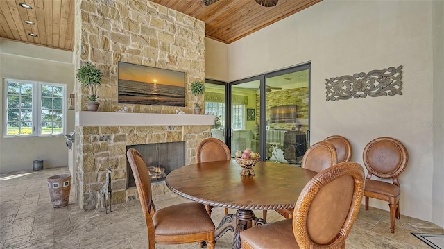 dining room featuring a stone fireplace, wooden ceiling, and a high ceiling