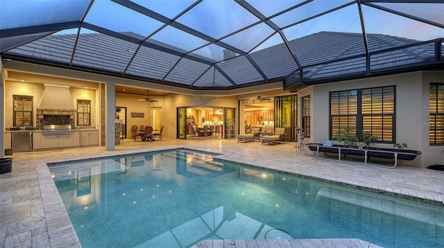 back house at dusk featuring ceiling fan, exterior kitchen, a patio, and glass enclosure