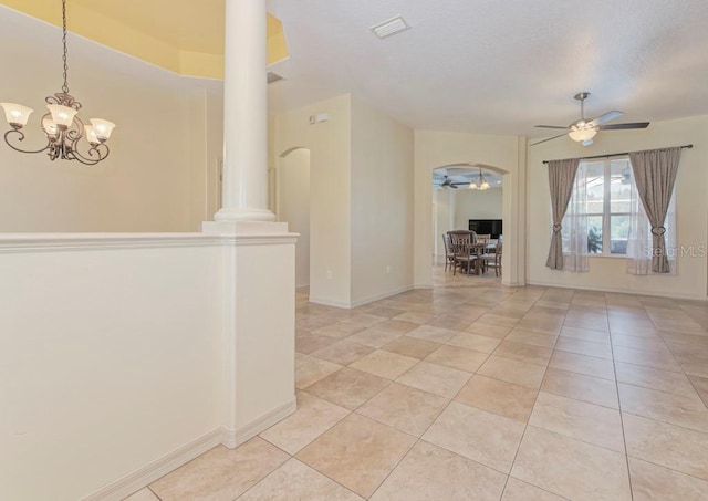 empty room featuring decorative columns, light tile patterned flooring, and ceiling fan with notable chandelier