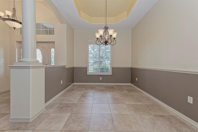 tiled spare room featuring a chandelier, ornate columns, and a tray ceiling