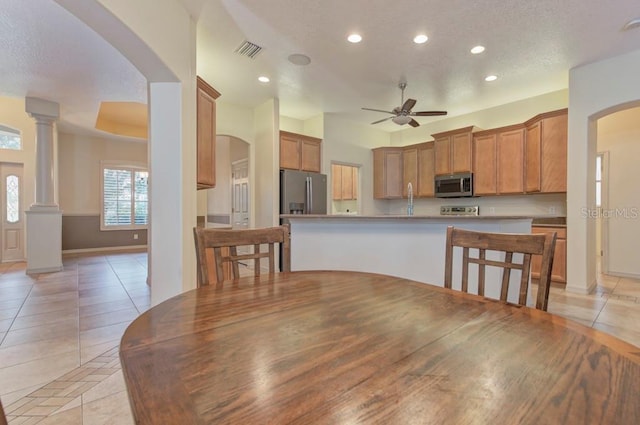 tiled dining space featuring decorative columns, a textured ceiling, and ceiling fan