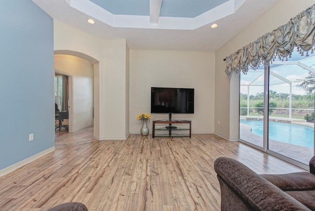 living room with light wood-type flooring and a raised ceiling