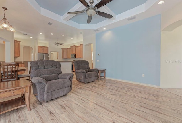 living room with light hardwood / wood-style flooring, ceiling fan with notable chandelier, and a raised ceiling