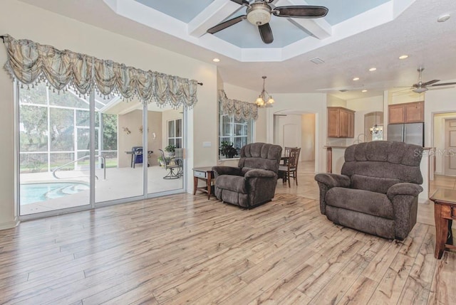 living room with light hardwood / wood-style flooring, a raised ceiling, and ceiling fan