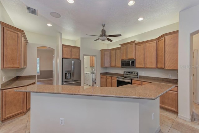 kitchen with stainless steel appliances, a center island, light stone counters, a textured ceiling, and ceiling fan