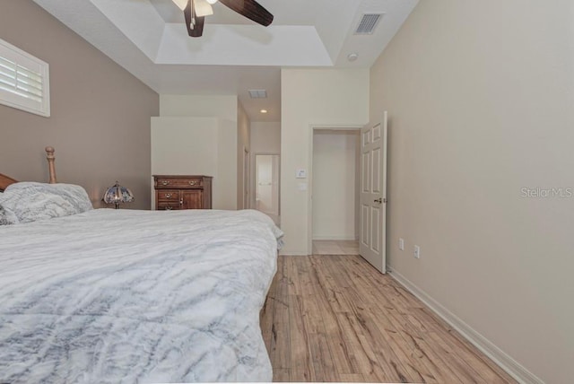 bedroom with light hardwood / wood-style flooring, a tray ceiling, and ceiling fan