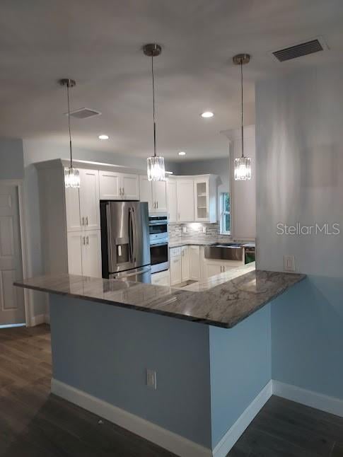 kitchen with dark hardwood / wood-style flooring, kitchen peninsula, white cabinetry, appliances with stainless steel finishes, and decorative light fixtures